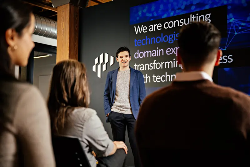 An Electric Mind team member presents to colleagues in front of a screen showing the company’s logo.